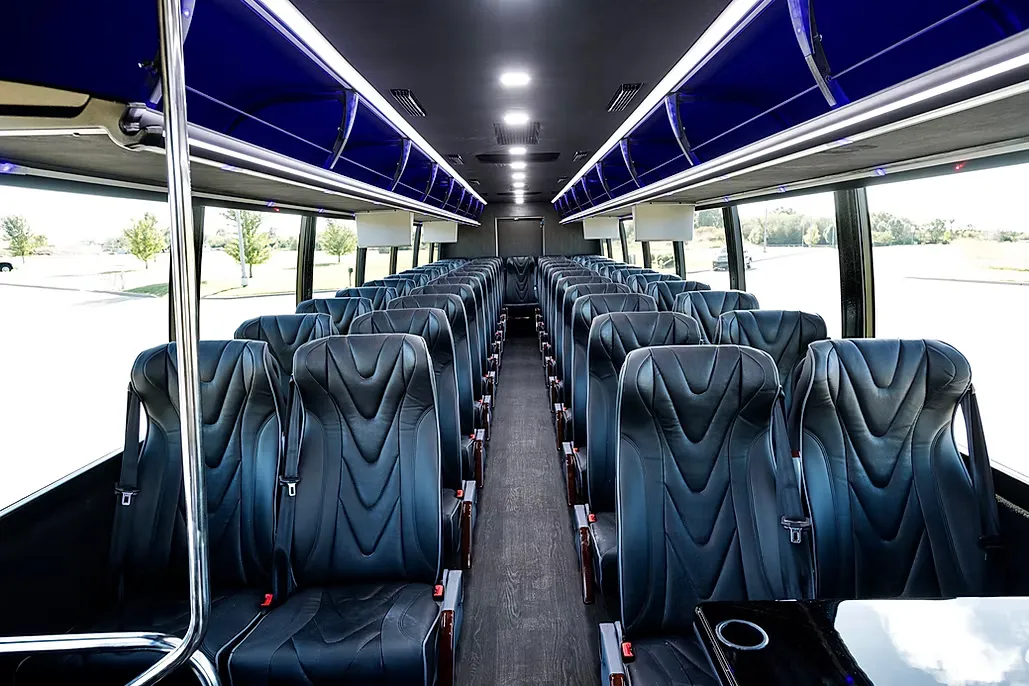 Interior of the Coach Bus: rows of black leather high-back reclining seats down both sides of a wood-floored aisle, seatbelts fitted